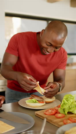 vertical video: preparing burger, man adding cheese slice to patty in kitchen