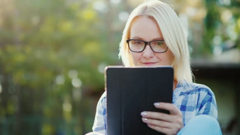 portrait of a young woman enjoying a tablet in the courtyard of her home concept - technology and di