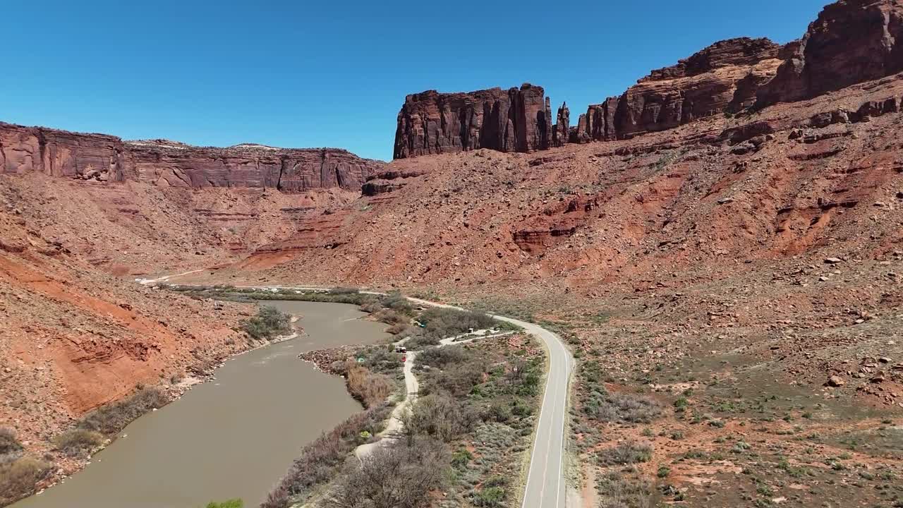 Drone Ascending Over Highway as Car Drives Down Road Next to River, Tall Vibrant Red Cliffs in Background, Highway 128, Moab Utah, Upper Colorado River Scenic Byway, early spring
