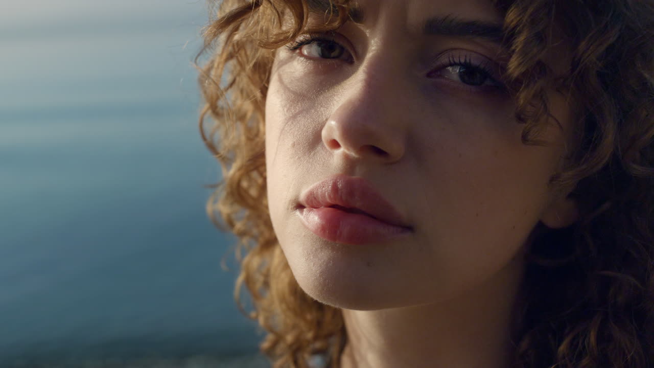 mujer triste posando ante la cámara en la playa. chica deprimida en primer plano parpadeando los ojos