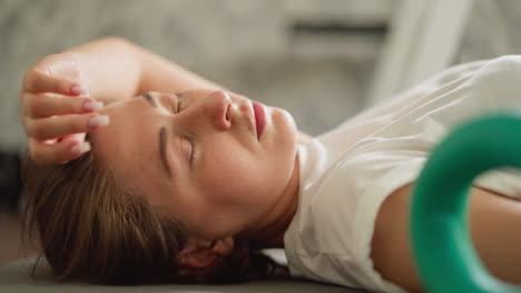 una mujer cansada descansa en el piso del gimnasio de primer plano. una mujer fatigada tiene migraña después de un duro entrenamiento en casa. una deportista toca la cabeza acostada en la alfombra en cámara lenta