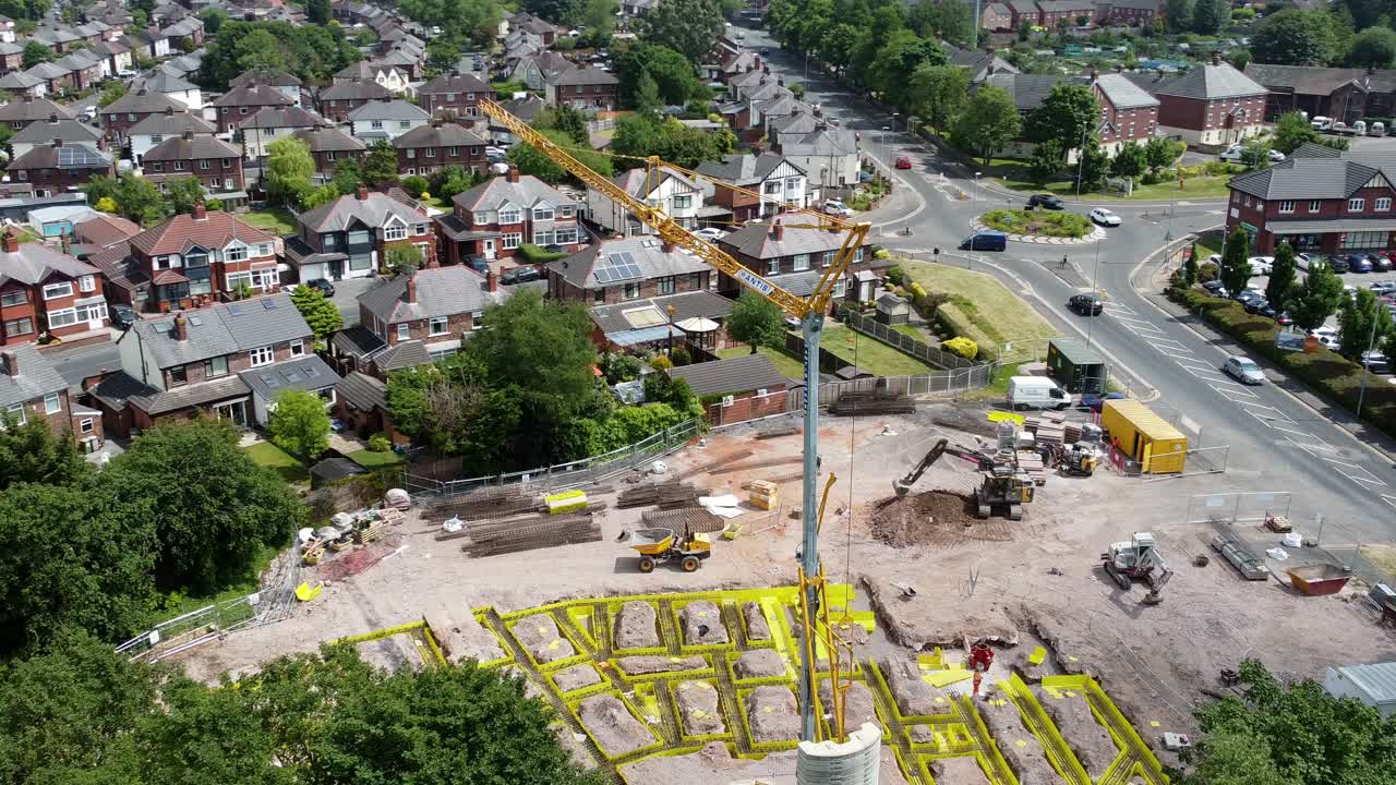 Tall crane setting building foundation in British town neighbourhood aerial circling view across suburban townhouse rooftops