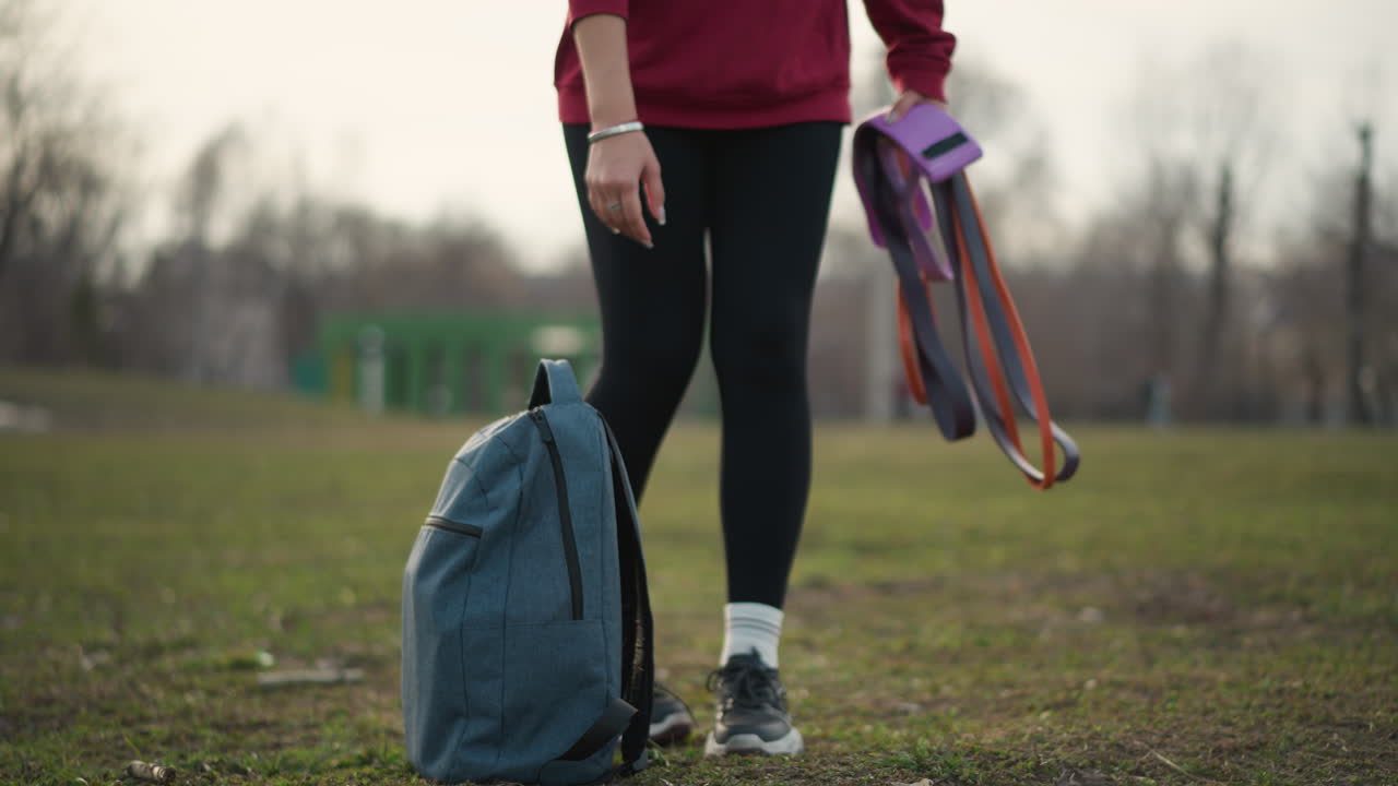 Woman Walking Outdoors, Colorful Straps On Backpack, Female In Sneakers Strolling Through Grassy Landscape, Woman With Bright Straps On Backpack Steps Across Lush Green Field In Daytime