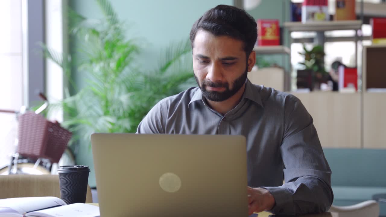 un hombre de negocios indio barbudo viendo un seminario en línea en una computadora portátil.