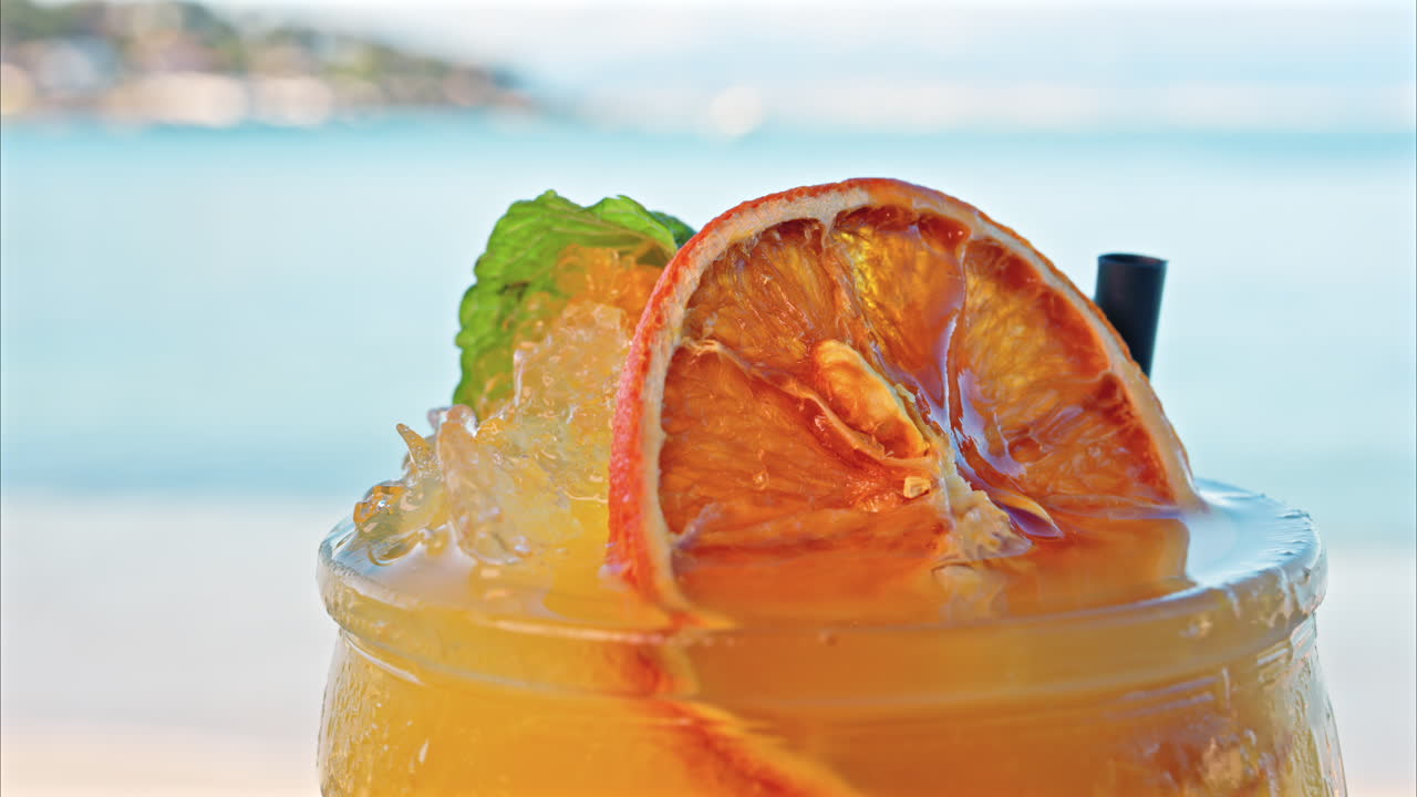 Close up of an orange cocktail on a table with a blurred view of the sea on the background