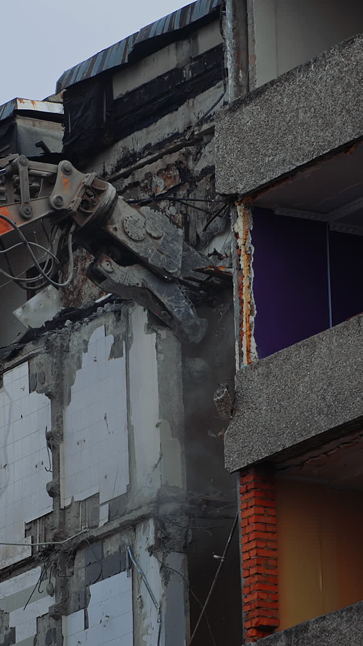 Bulldozer claw grab the concrete wall in order to break it. Demolishing the building wrecked by an earthquake. View from below. Vertical video
