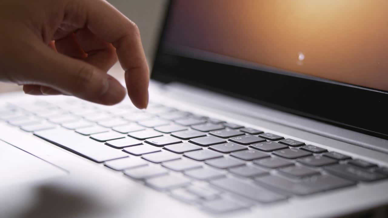 Index finger pressing laptop key, activating white cursor on orange screen for tech while lifting