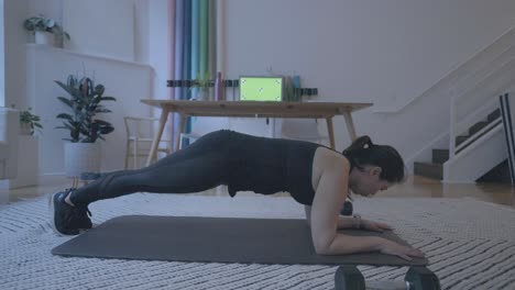 A-static-shot-of-a-woman-holding-a-plank-in-front-of-a-computer-green-screen-at-her-home-in-her-living-room-4k60