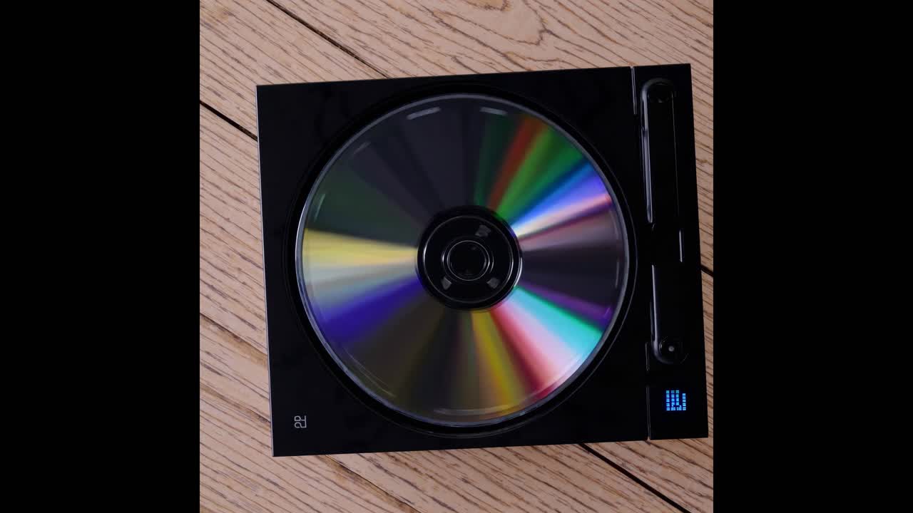Ovenfra og ned-visning av en snurrende CD i en spiller på tregulv, som viser et retro videokonsept