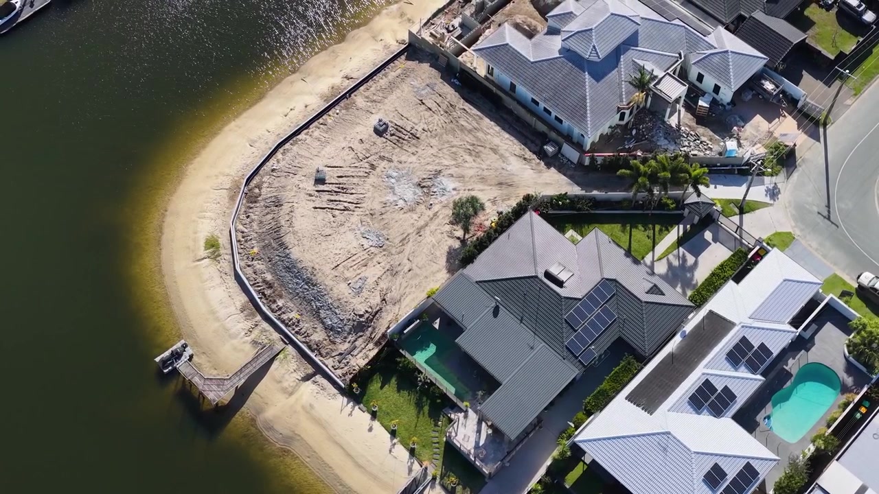 High-angle drone shot reveals upscale canal homes and a vacant lot under development.