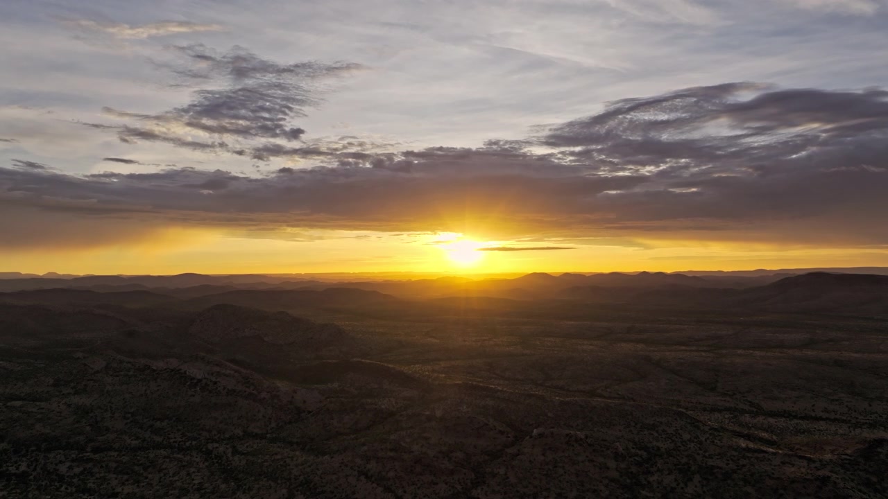 Riprese con drone di un'alba dorata sulla vasta distesa desertica della Namibia centrale, luce calda che inonda le pianure sotto un cielo nuvoloso.