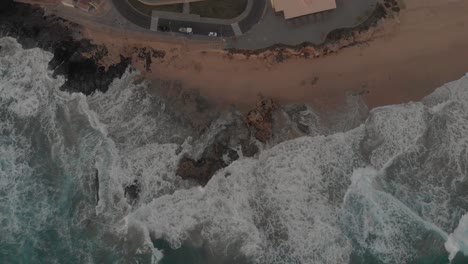 Punto-De-Vista-Aéreo-De-Arriba-Hacia-Abajo-Del-Océano-Agitado-Y-Las-Olas-Rompiendo-En-La-Playa,-Ponta-Da-Calheta