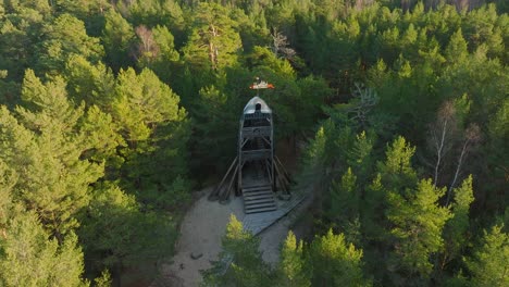 vista aérea de pájaro de la moderna torre de observación en forma de barco en medio del bosque de pinos, bosque nórdico, sendero forestal, tarde soleada, luz de la hora dorada, amplia toma de drones avanzando