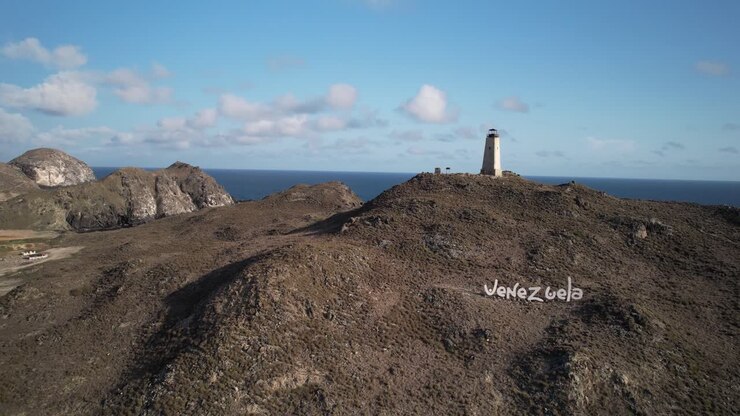 Faro di El Gran Roque su una collina scoscesa con lo sfondo dell'oceano sotto un cielo sereno, vista aerea.