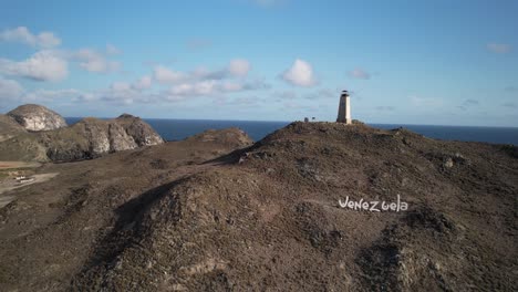 el gran roque lighthouse on a rugged hill with ocean backdrop under a clear sky, aerial view