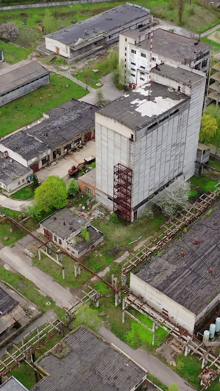Large territory of abandoned plant. Damaged buildings of an old factory. Ruined industry in springtime. Aerial view. Vertical video