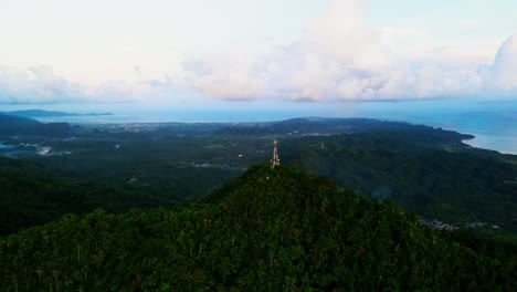orbiting aerial view of lush, mountainous terrain of mount cagmasuso with phone telecommunications tower overlooking provincial town san andres, catanduanes.