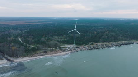 estableciendo una vista aérea de los edificios fortificados abandonados a la orilla del mar en los fuertes del norte de karosta en la playa del mar báltico en liepaja, día nublado, turbina eólica, disparo de órbita de avión no tripulado