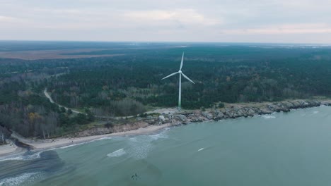 establishing aerial view of abandoned seaside fortification buildings at karosta northern forts on the beach of baltic sea in liepaja, overcast day, wind turbine, drone orbit shot