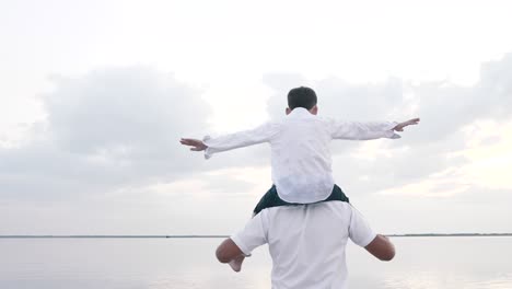 father carrying on shoulders son, walks together, plays fun plane game outdoors
