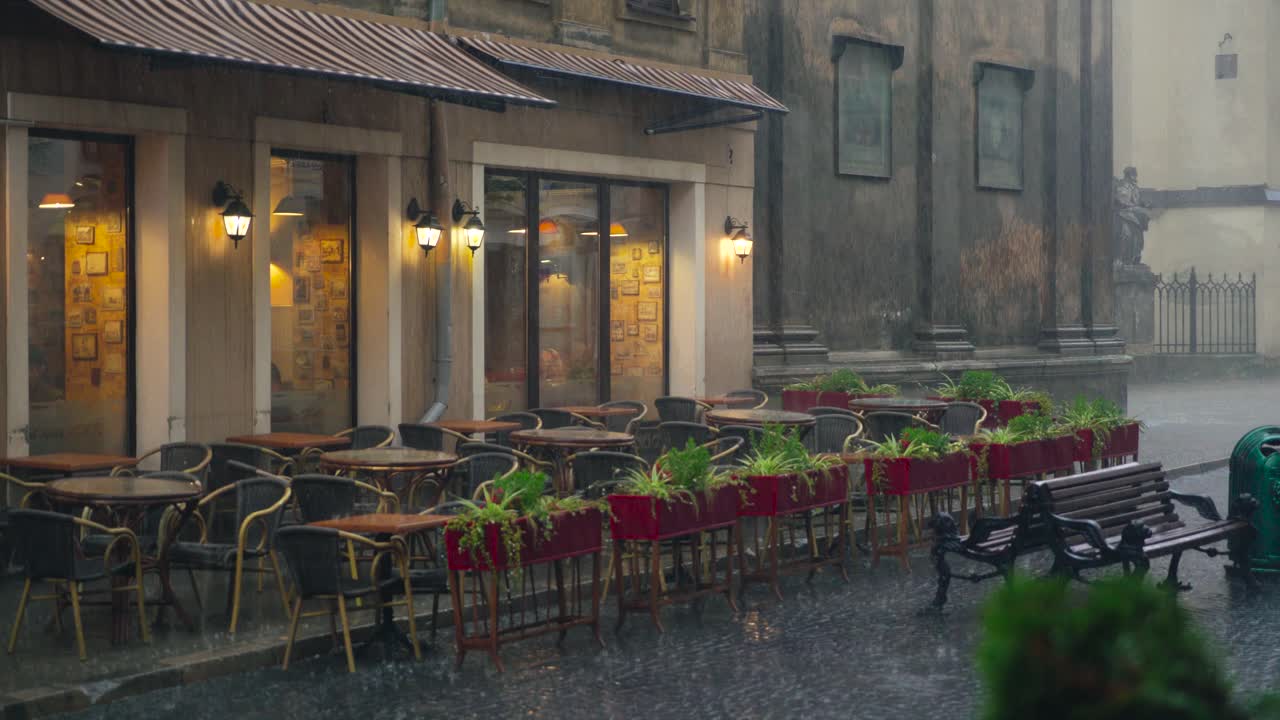 view on a wet summer terrace of the cafe with flowers, tables and chairs in the street in rainy weather. It's raining cats and dogs