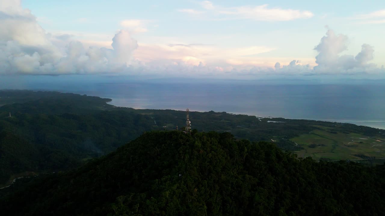 Panoramic aerial flyover shot of Mount Cagmasuso summit and Telecommunications tower overlooking tropical island horizon during dusk - Catanduanes, Philippines