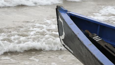 closeup of currach boat front keel or bow with faded number on front, ocean waves crash