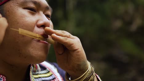 close up shot of an indigenous person playing kubing tribal instrument, behind is a waterfall