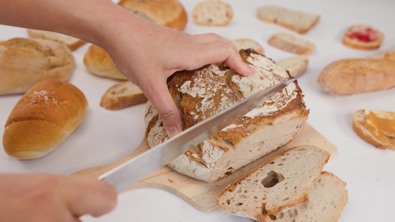 Close-up of hands using a knife to slice crusty artisanal bread on a white surface.