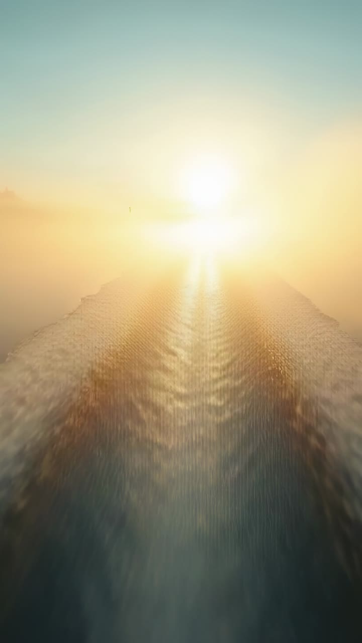 Vertical video: Moving boat creating V-shaped wake heading toward low sun over open water haze