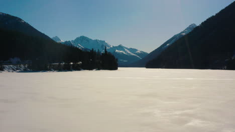 Aerial-fly-over-frozen-lake-with-dramatic-mountain-vista-behind