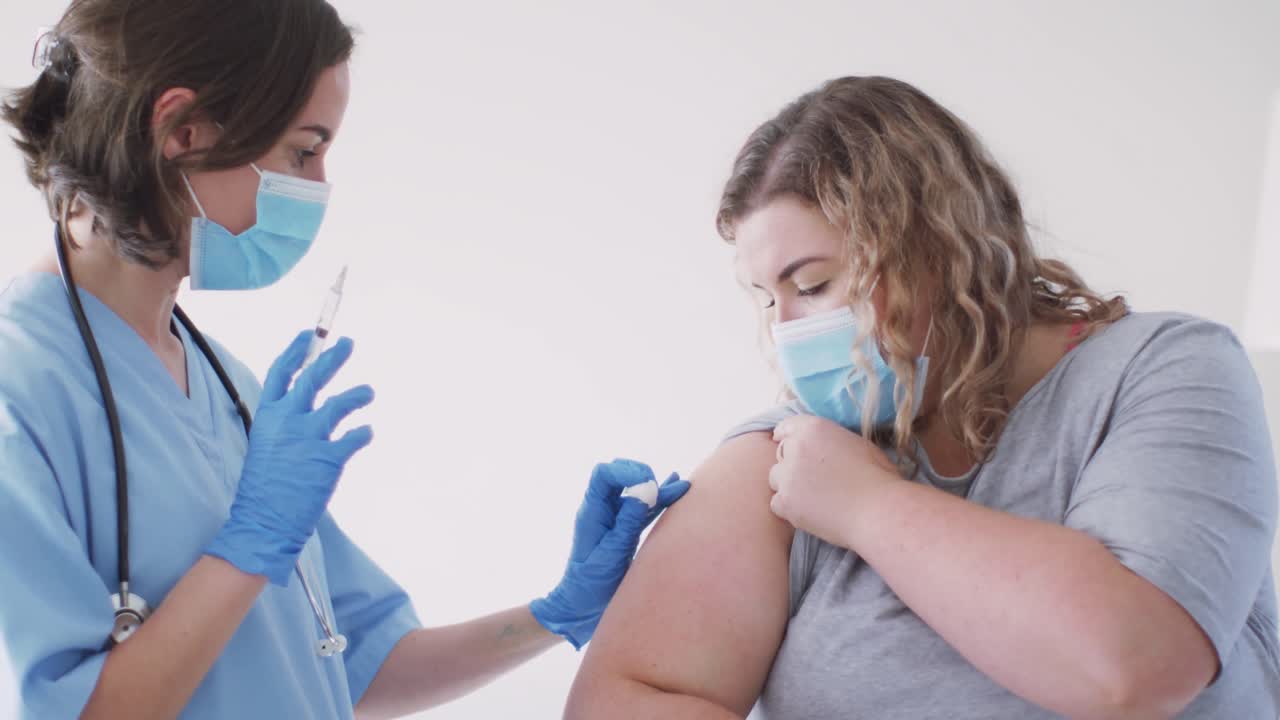 mujer caucásica y doctora caucásica con máscara facial en casa vacunando