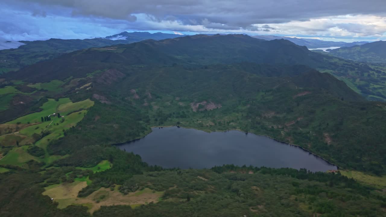 Drone pans above Pantano Redondo lake surrounded by forested Andean hills