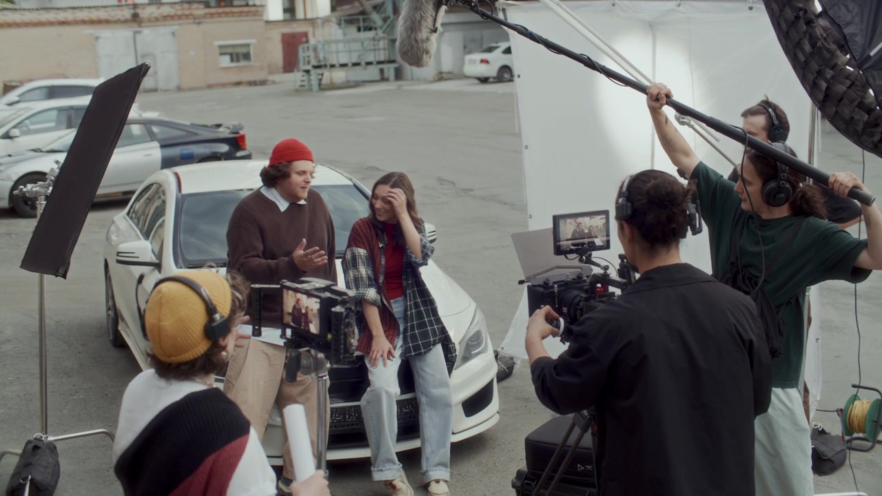 Film Crew Capturing Actors Chatting by Car Hood on Urban Movie Set