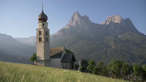 perfect old church building in a green valley in the mountains on a sunny day sliding shot, ortisei, south tirol, italy