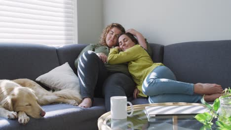 caucasian lesbian couple smiling and sitting on couch with dog