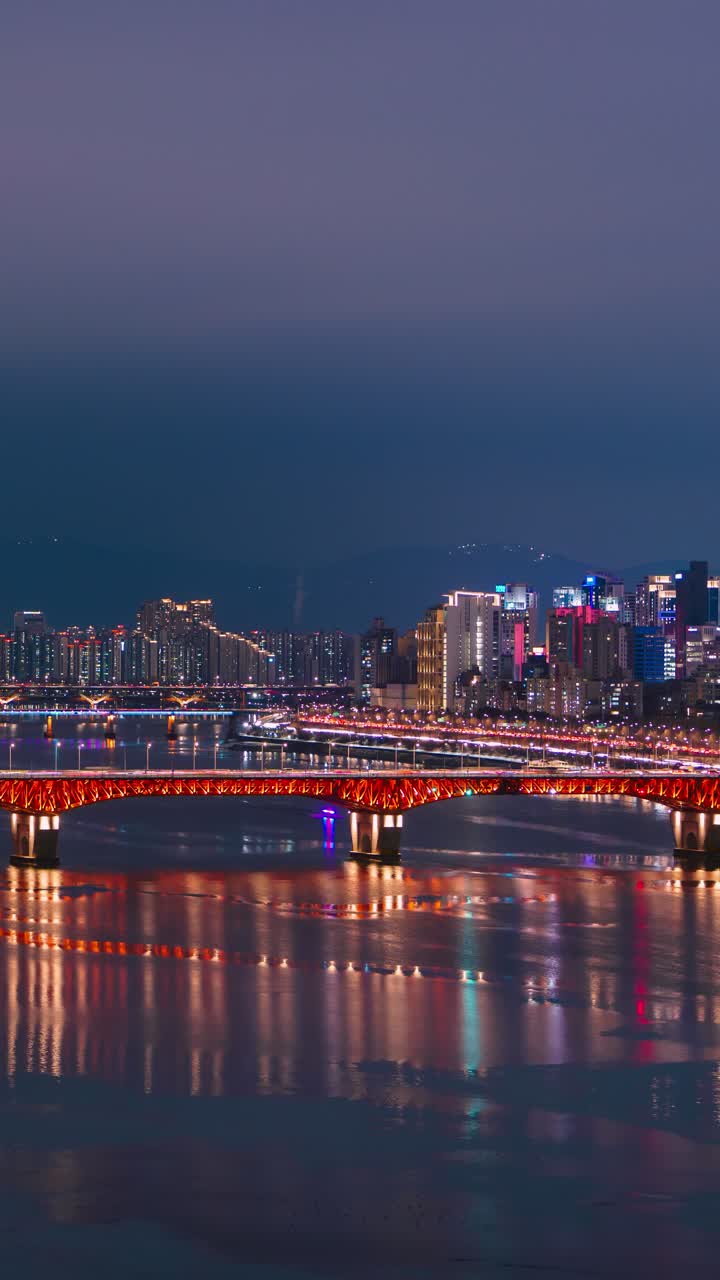 Un time-lapse aereo verticale cattura il ponte Seongsu sul fiume Han con i riflessi dei semafori di Olympic-daero nell'ora blu invernale del paesaggio urbano di Seoul con gli appartamenti illuminati di Gangnam e la montagna in lontananza