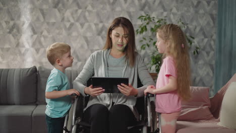 los niños se paran cerca de la madre en silla de ruedas viendo videos
