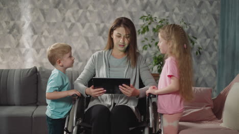 children stand near mother in wheelchair watching videos