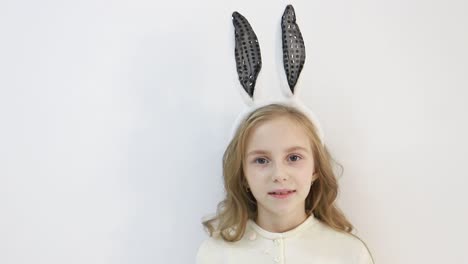 smiling little girl in a cloak, dressed in the ears of an easter bunny, a happy child is waiting for the holidays, on a white background