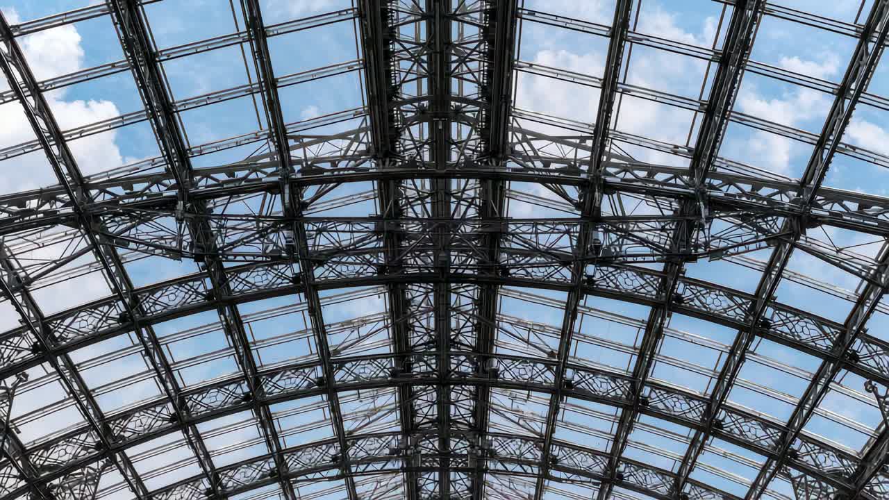 Inclinazione della camera che rivela la griglia del tetto in acciaio e vetro alla stazione, mostrando la nervatura centrale, nuvole alla deriva