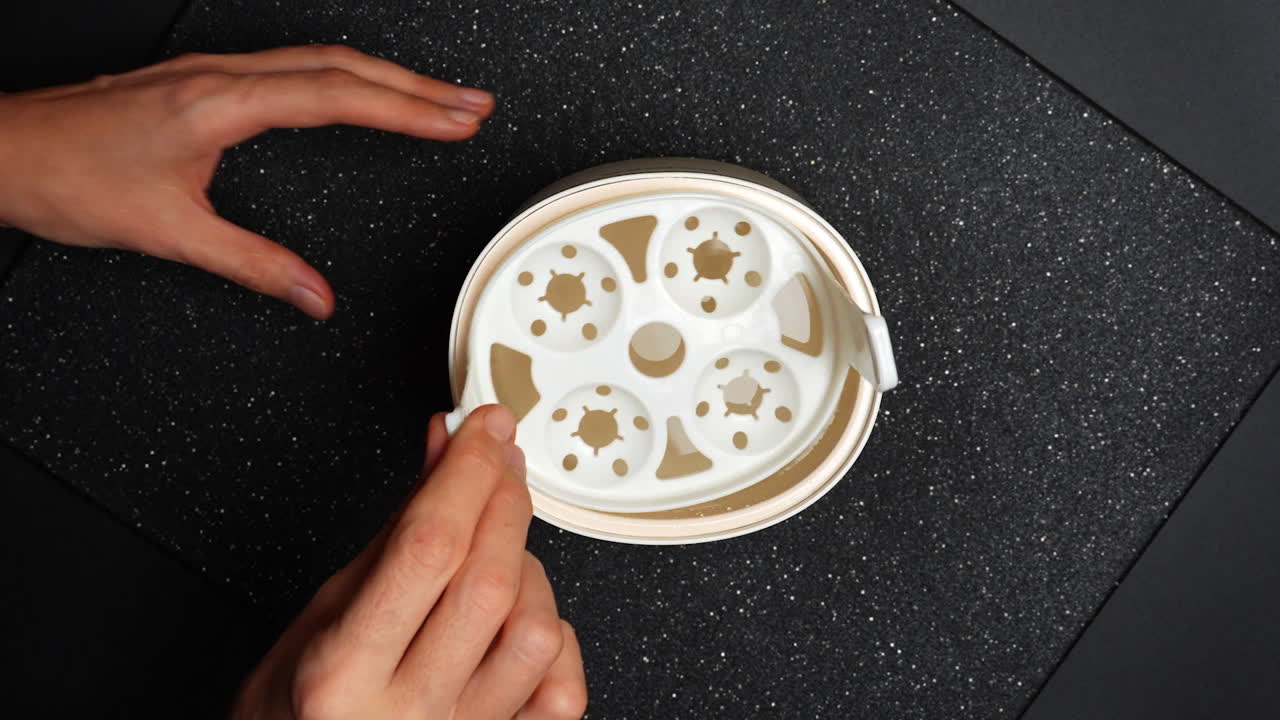 Una persona tiene in mano un contenitore rotondo pieno di liquido su una superficie scura. Una persona tiene in mano un contenitore rotondo pieno di un liquido cremoso su una superficie scura piatta