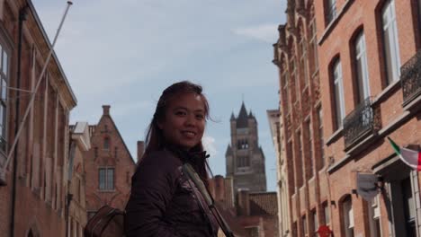 woman smiling in front of historic building in bruges, belgium on a sunny day