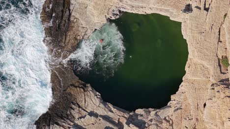 dramatic top-down drone footage at giola in thasos as a sudden wave sweeps a man near the edge of the natural pool, narrowly avoiding an accident