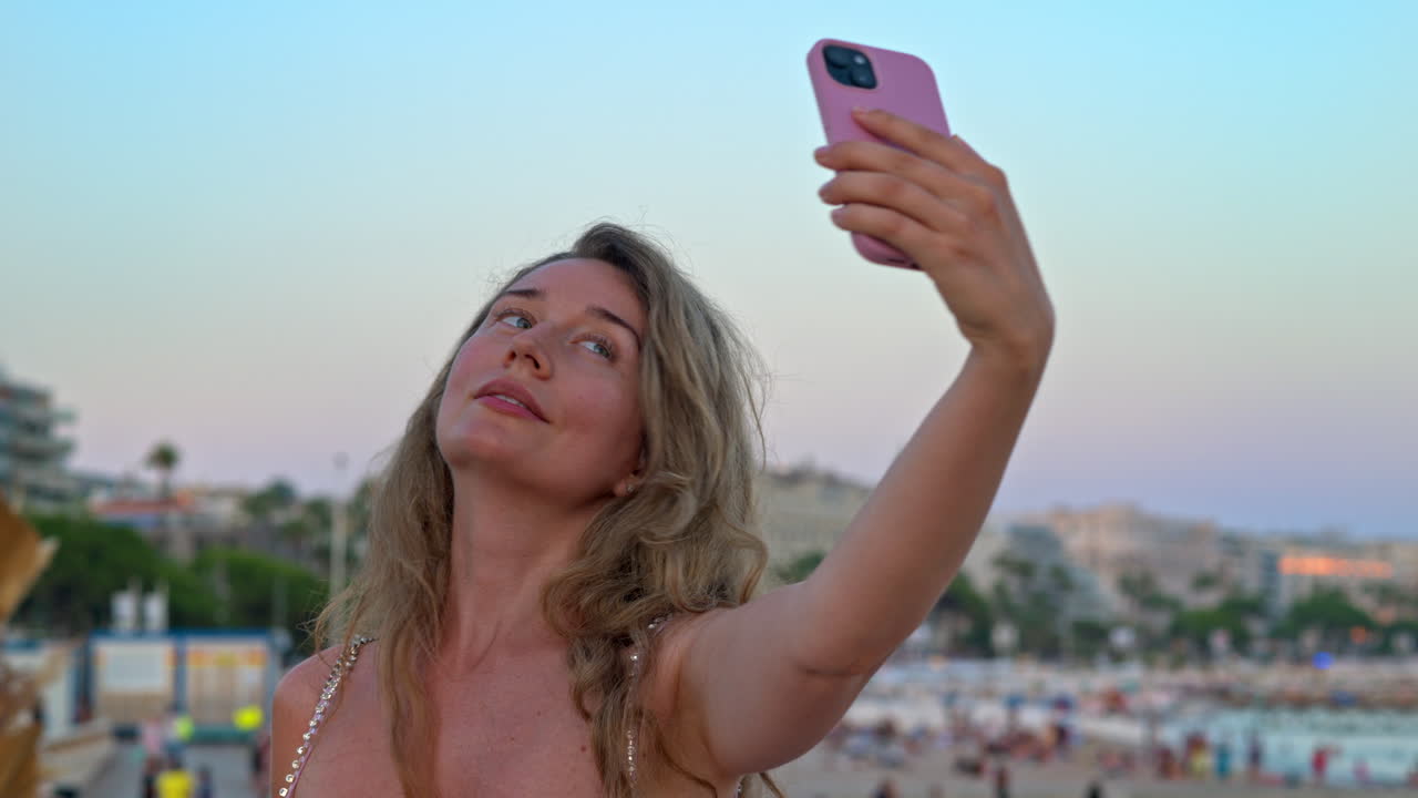 Donna con un vestito rosa che scatta foto sulla spiaggia di Cannes, in Francia, di sera