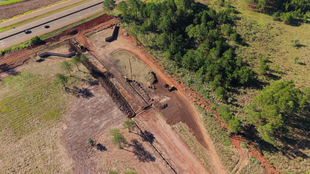 Road construction site with machines clearing land and trees nearby, aerial view