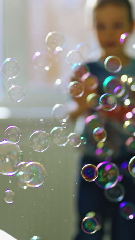 boy having fun at home. young boy having fun with soap bubble at home vertical video