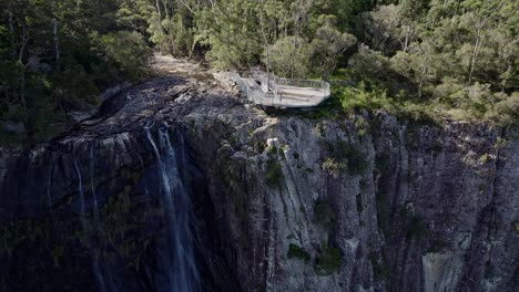 Mujer-Saludando-Desde-El-Mirador-De-Minyon-Falls-Con-Vistas-A-La-Cascada-Y-La-Selva-Tropical-En-La-Región-De-Los-Ríos-Del-Norte-De-Nueva-Gales-Del-Sur