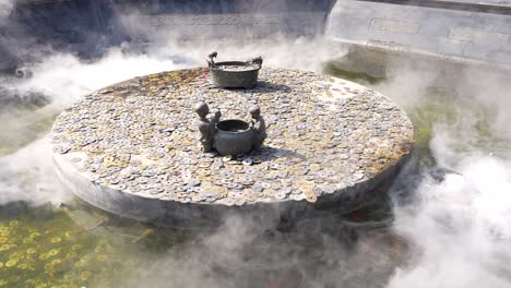 estanque budista con una rueda de piedra cubierta por monedas con nebulización