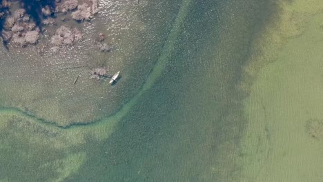 High-overhead-drone-shot-of-man-in-canoe-rowing-in-lake-with-sparkling-waters